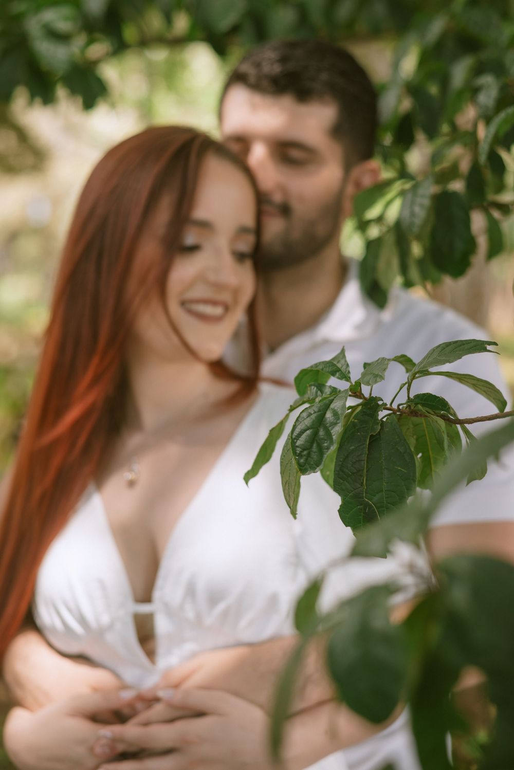 An intimate couple's portrait amidst green foliage in soft focus.