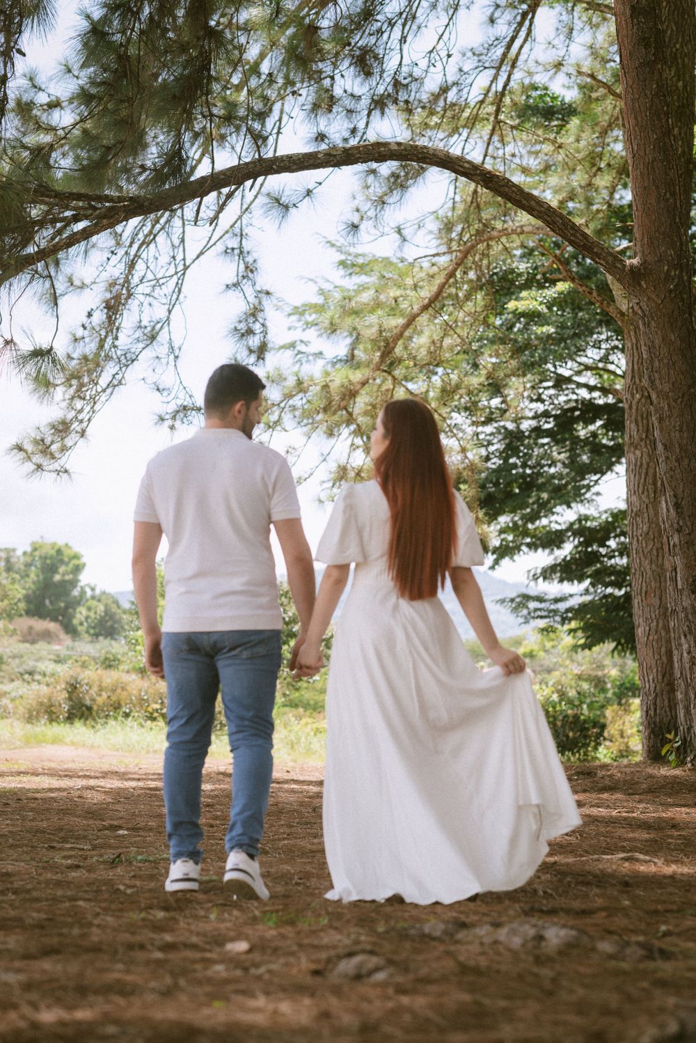 A couple walking hand in hand down a forest path in matching white outfits.