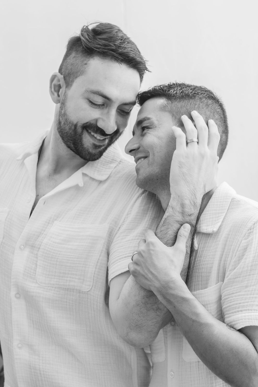 Intimate black and white portrait of two people in white shirts sharing a tender moment.