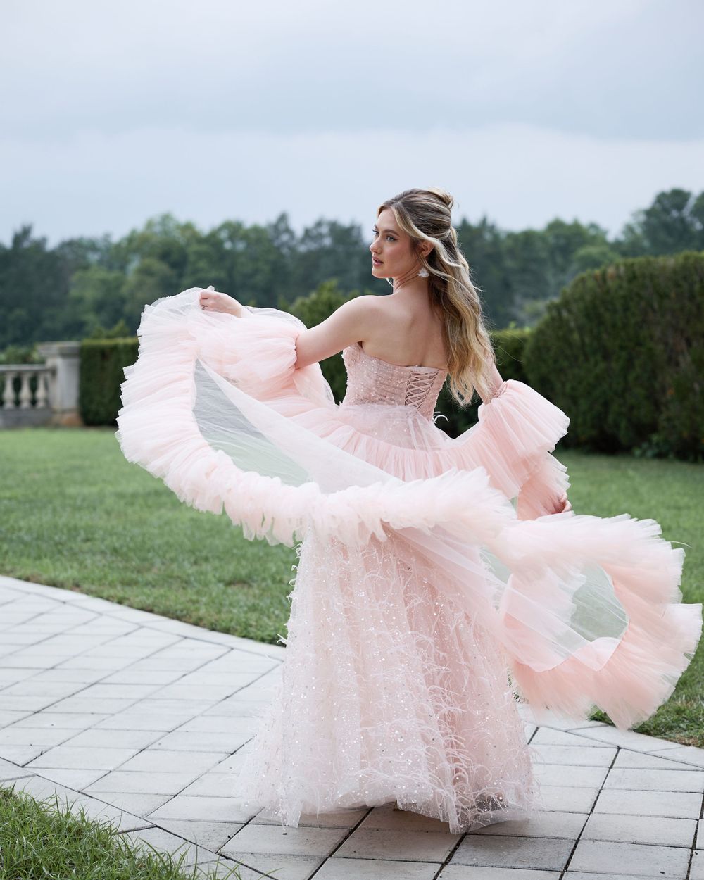 Twirling bride in flowing pink tulle gown on stone terrace with garden background.