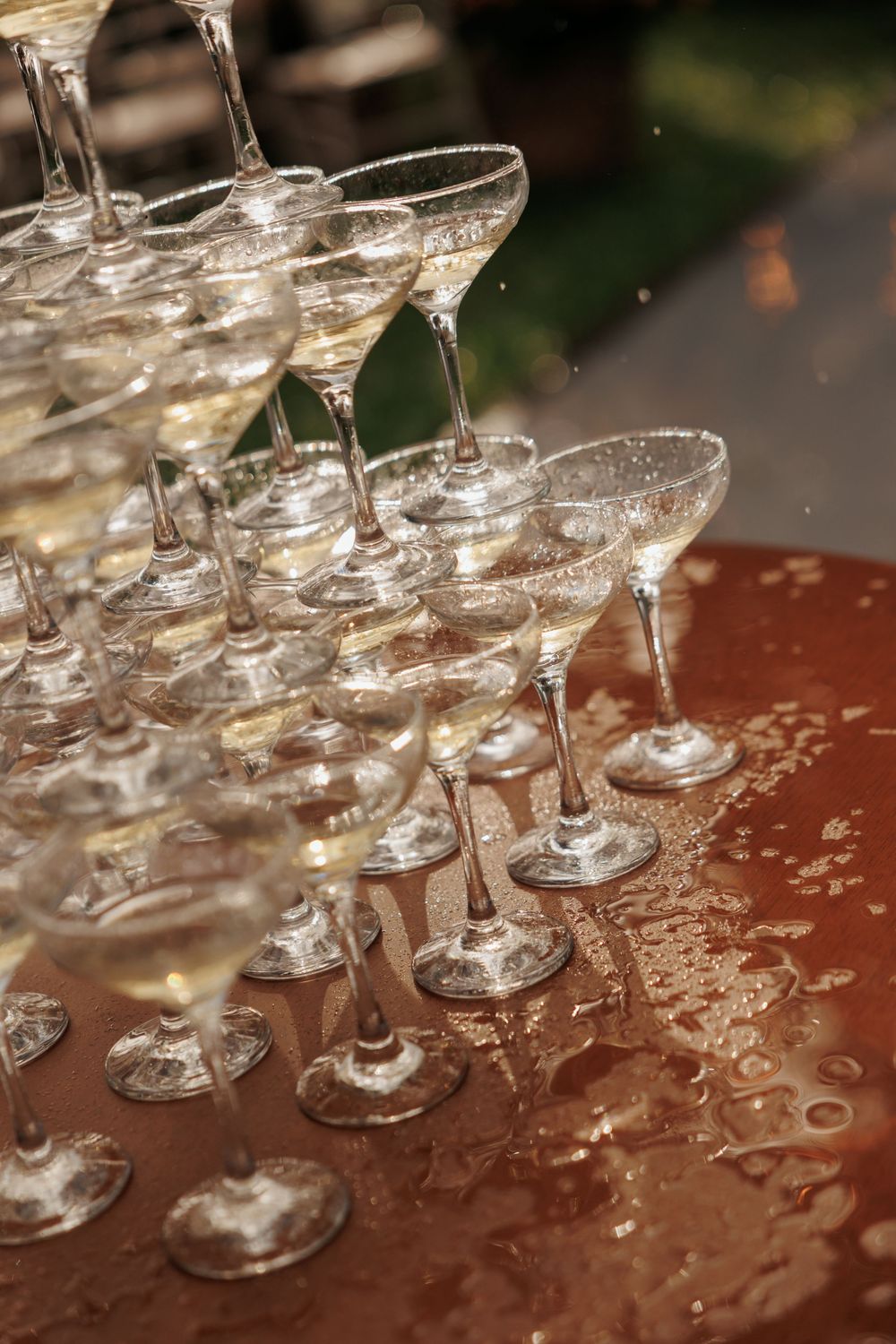 Elegant champagne tower with coupe glasses filled with sparkling wine on a wet reflective table at a celebration event.