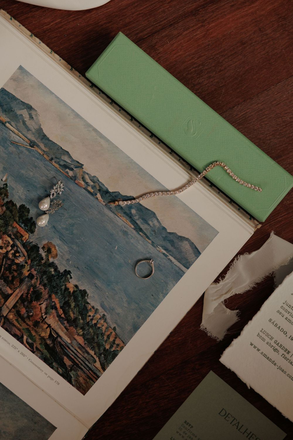 Wedding details including rings and jewelry displayed with a landscape photo on wooden surface.