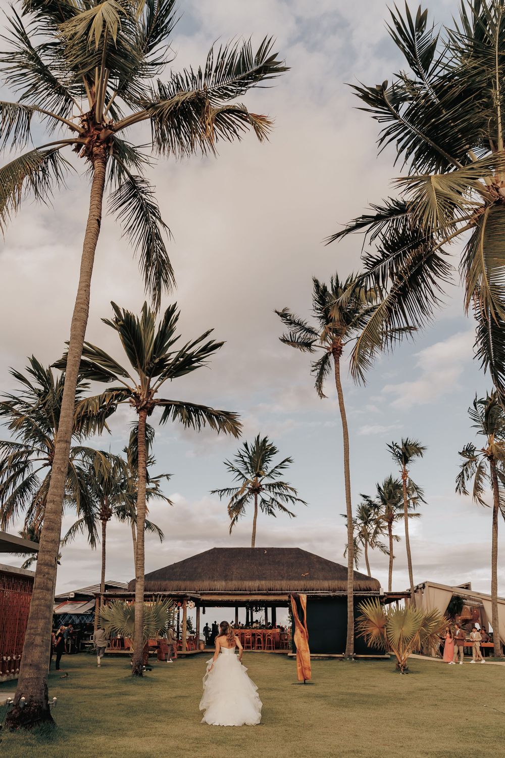 Palm trees frame tropical wedding venue with gazebo under cloudy sky.