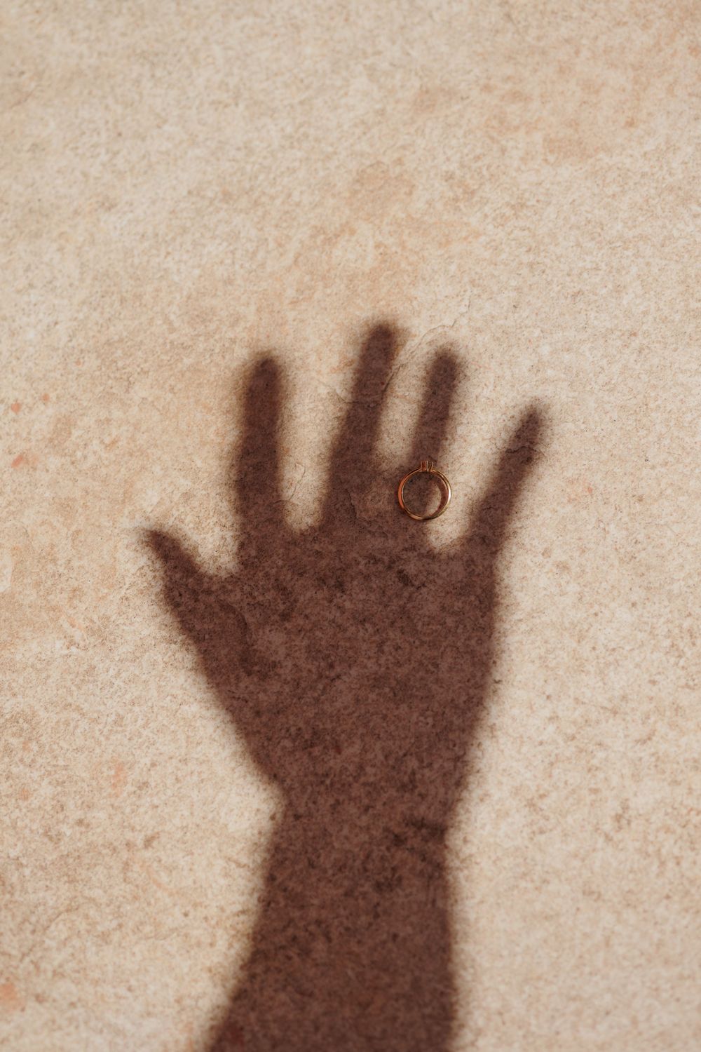 Shadow of a hand with a gold ring on a beige stone surface.
