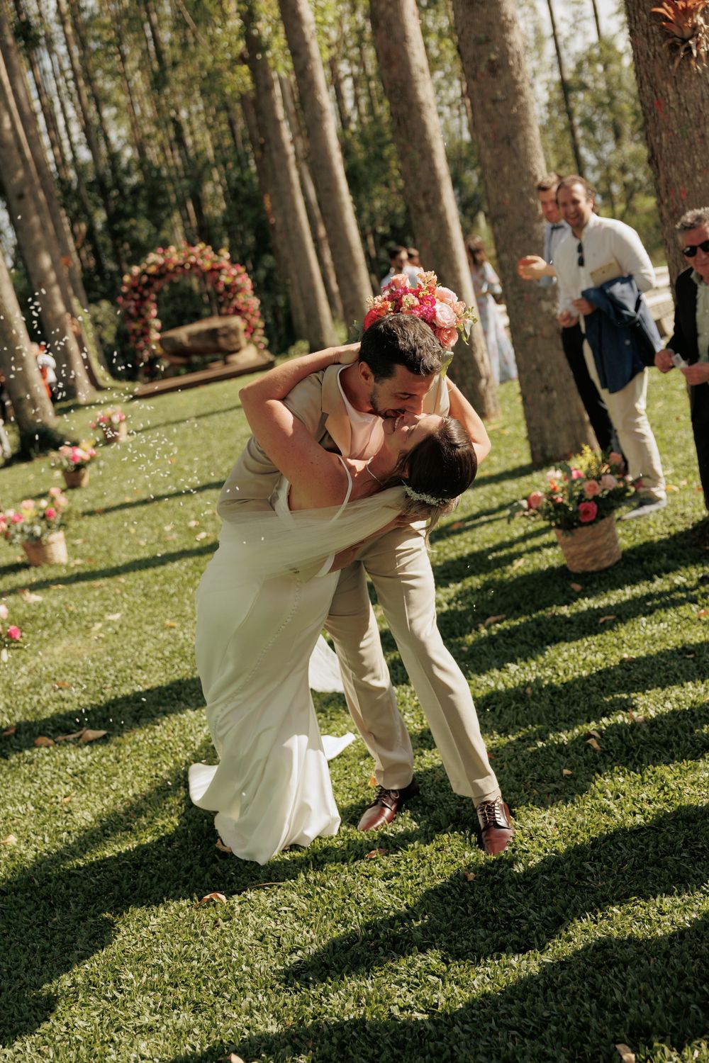 Romantic dip kiss between newlyweds in sunny garden with floral decorations.