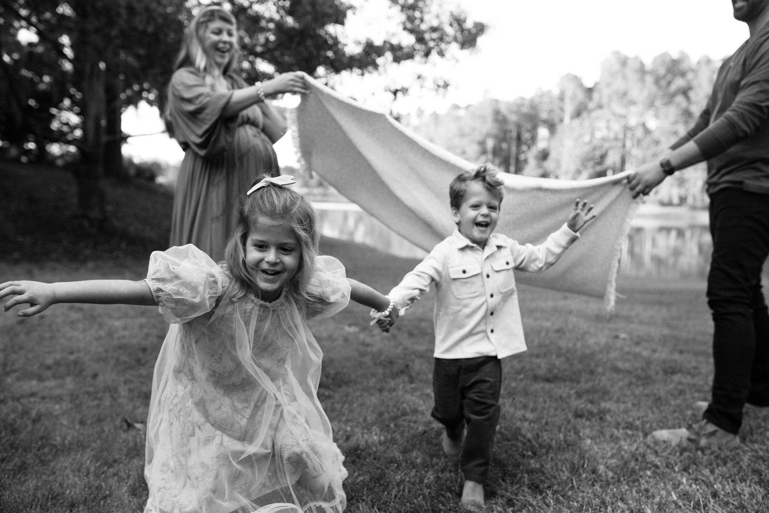 Children run and play in a yard with adults holding a large sheet or blanket in black and white photography by B. Logsdon in Savannah, GA.