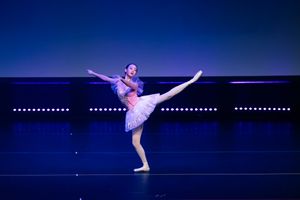 Solo ballet dancer in tutu performing arabesque pose on dark stage.