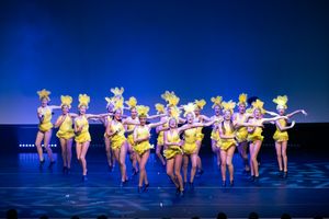 Dance performers in yellow costumes perform a synchronized routine on a stage with blue lighting effects.