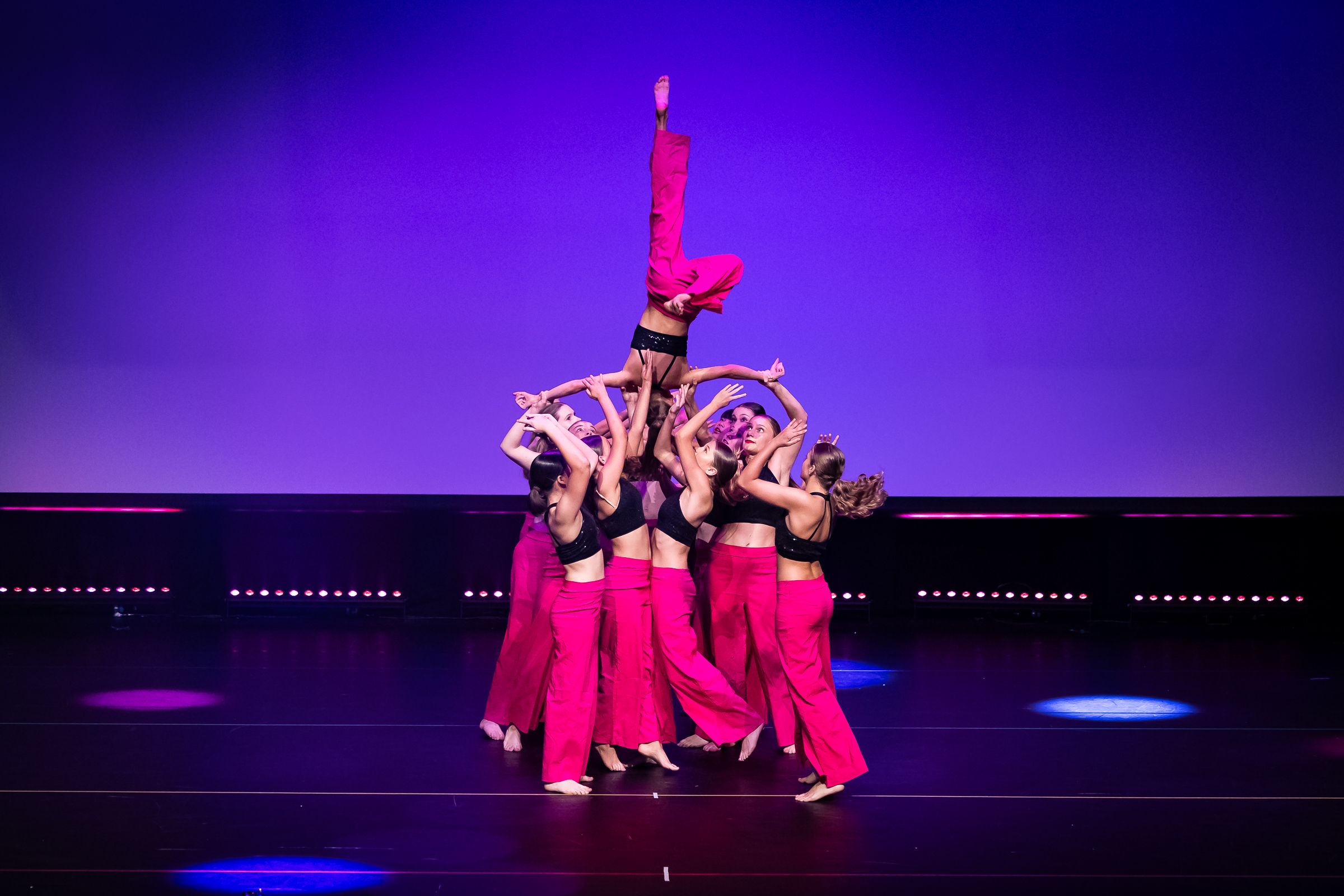 Dance performance featuring group lift on purple-lit stage with dramatic lighting.