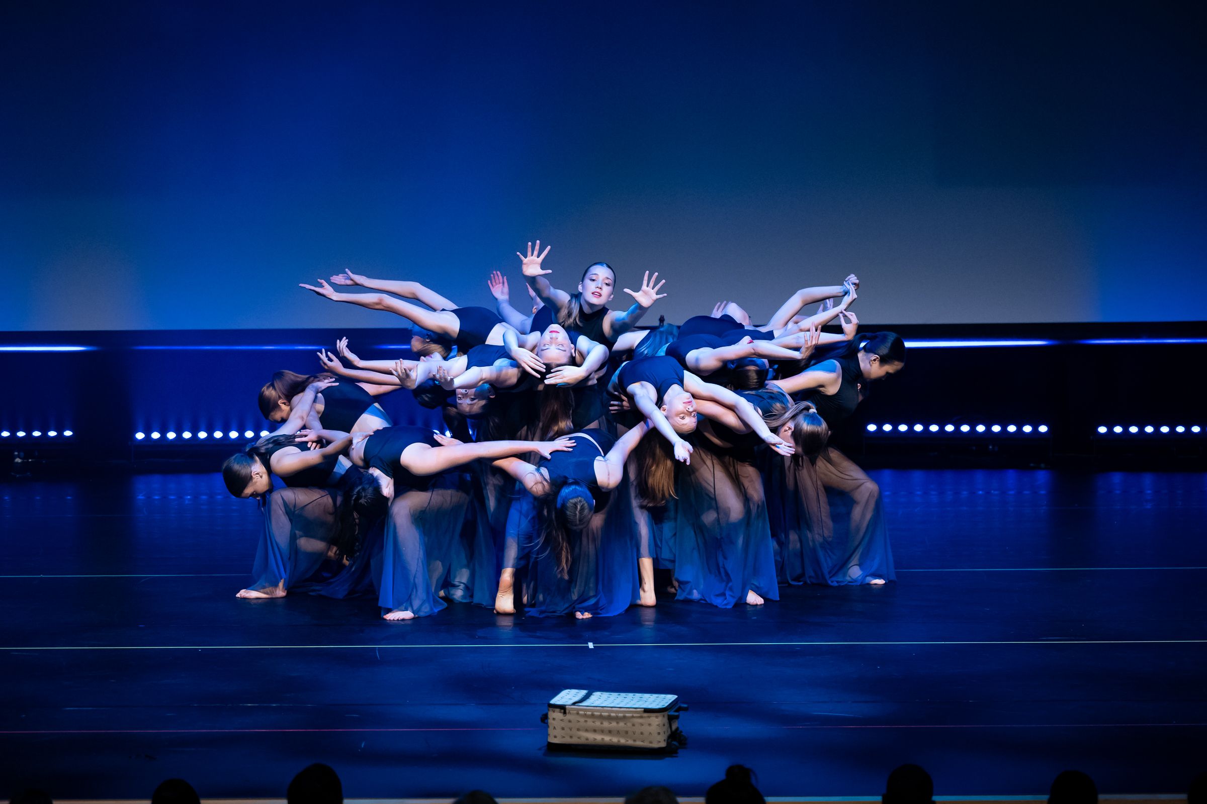 Modern dance ensemble performing in blue lighting on dark stage.