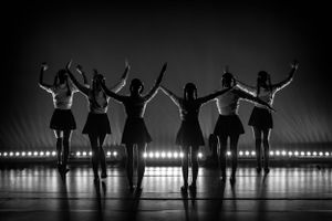 Silhouetted dancers pose with raised arms against stage lighting.
