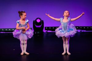 Two young ballet dancers in purple tutus perform on stage.