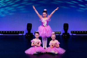 Three dancers in pink tutus strike graceful poses during stage performance.