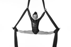 Aerial performer doing splits while suspended on black silk ribbons.