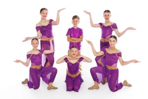 Dance group in matching purple outfits striking synchronized poses in studio setting.