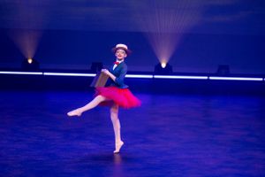 Dancer in blue top and red tutu performs solo on illuminated stage.