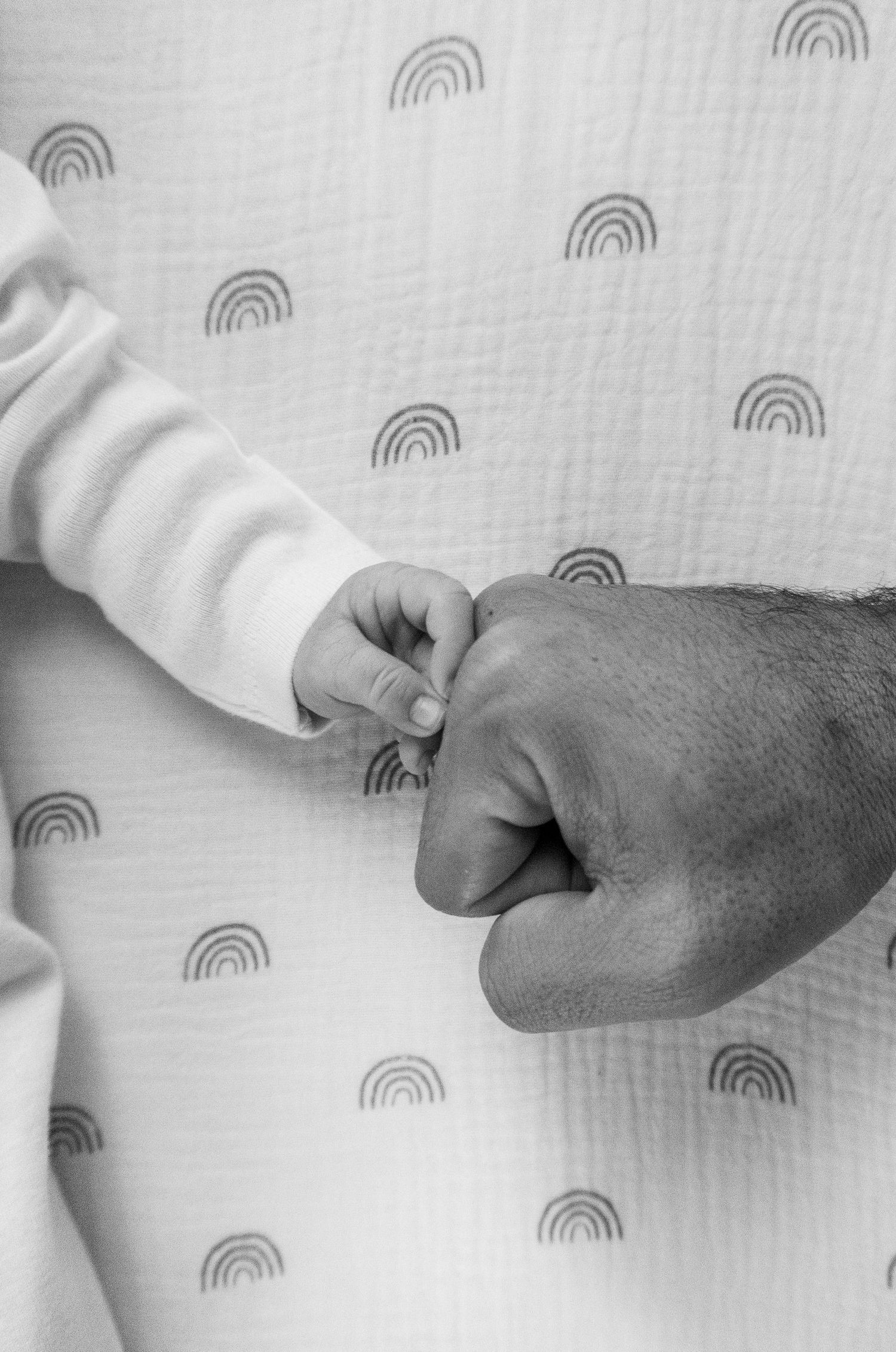 Black and white image of baby and dad fist bumping with rainbows in the background