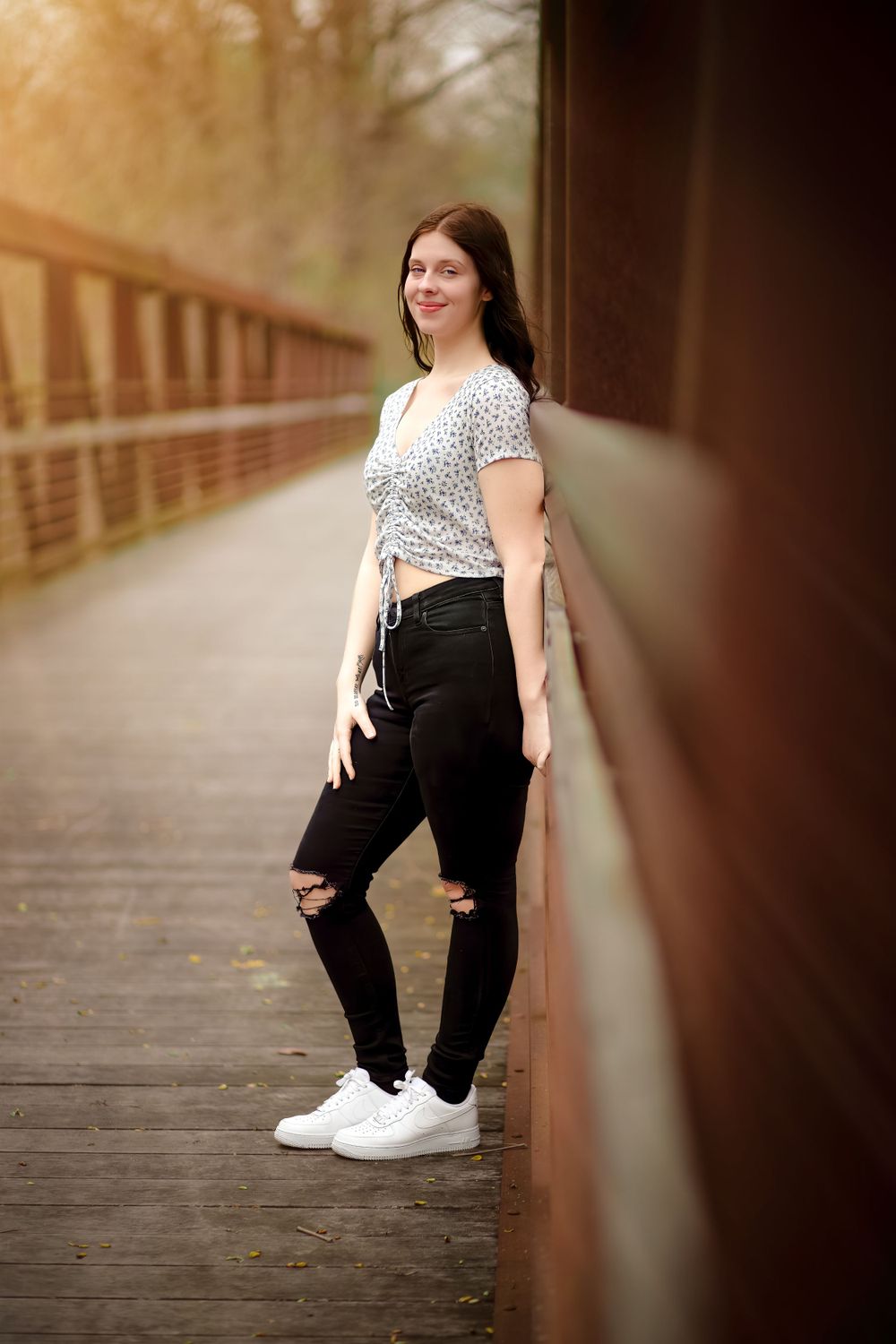 Casual portrait on wooden bridge wearing polka dot top and ripped jeans.