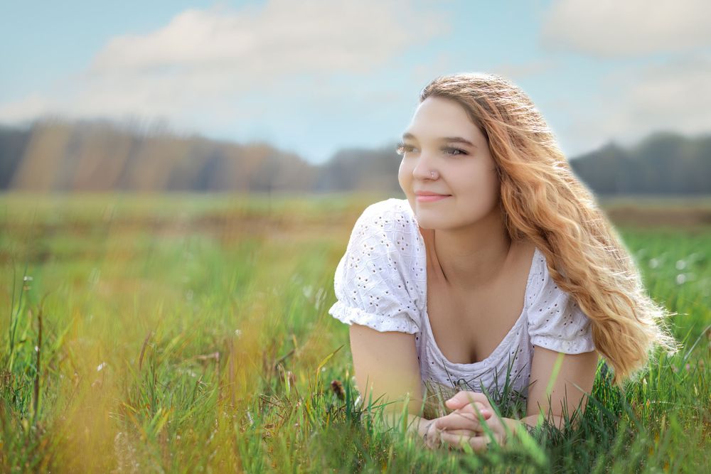 Portrait in meadow with white lace top against natural summer field backdrop.