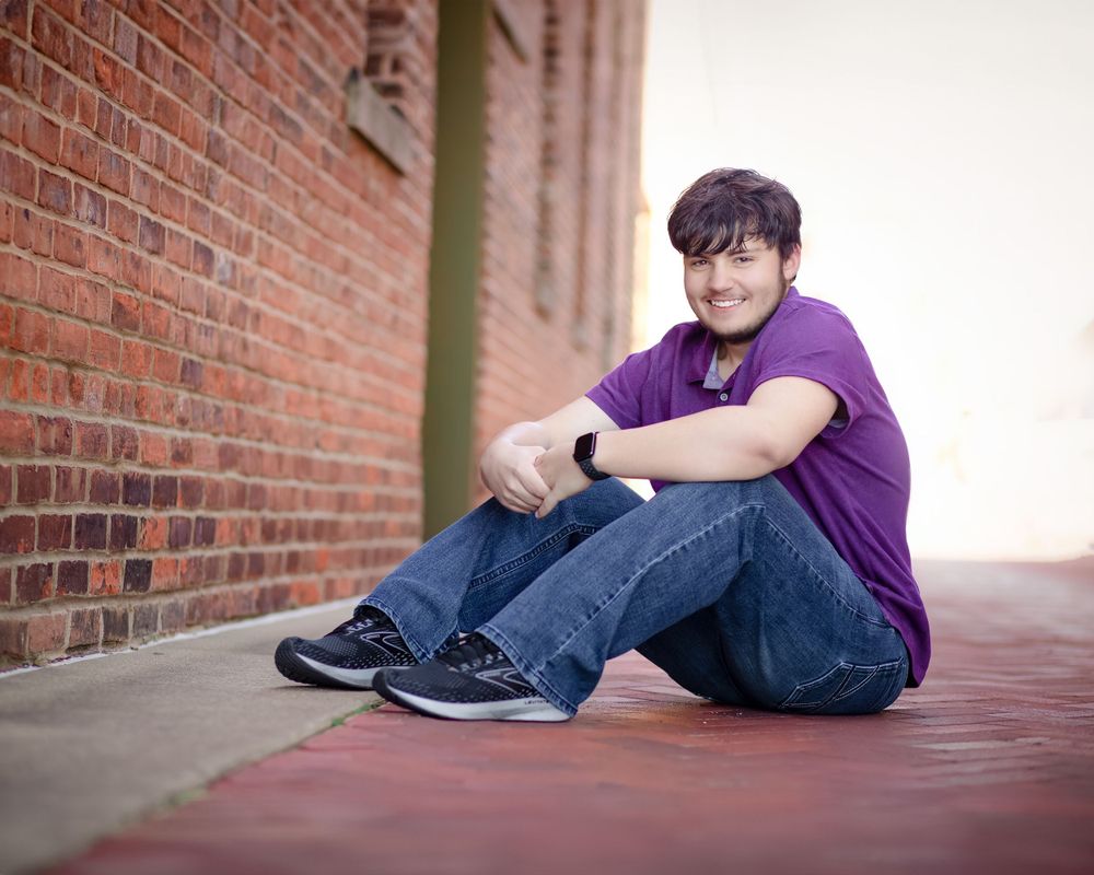 Person wearing purple polo shirt sitting against brick wall.