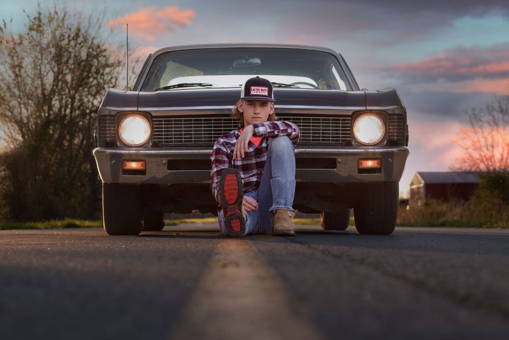 Classic vintage Chevrolet Nova photographed at sunset with figure kneeling in front.