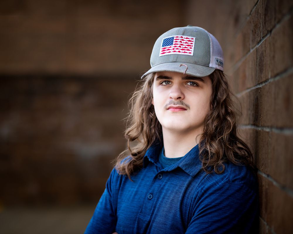 Portrait against brick wall featuring American flag baseball cap and blue collared shirt.