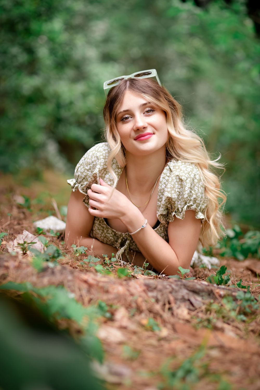 Portrait in vintage-style dress lying on ground with sunglasses in outdoor setting.