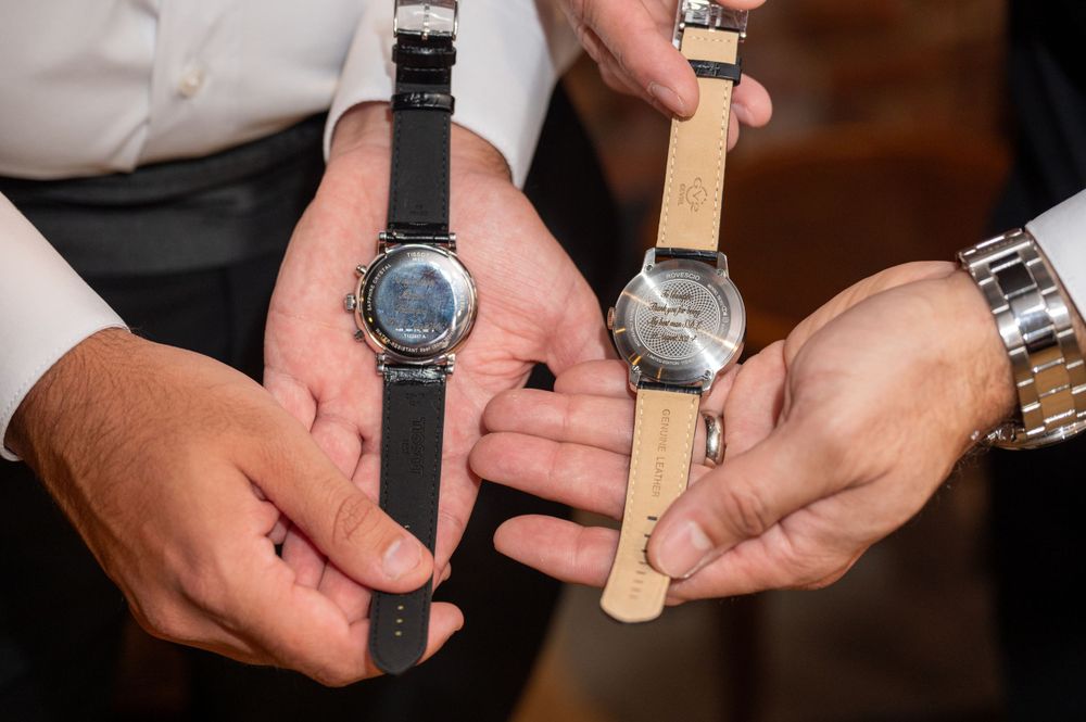 Two grooms exchanging engraved wedding watches as heartfelt gifts before their ceremony.