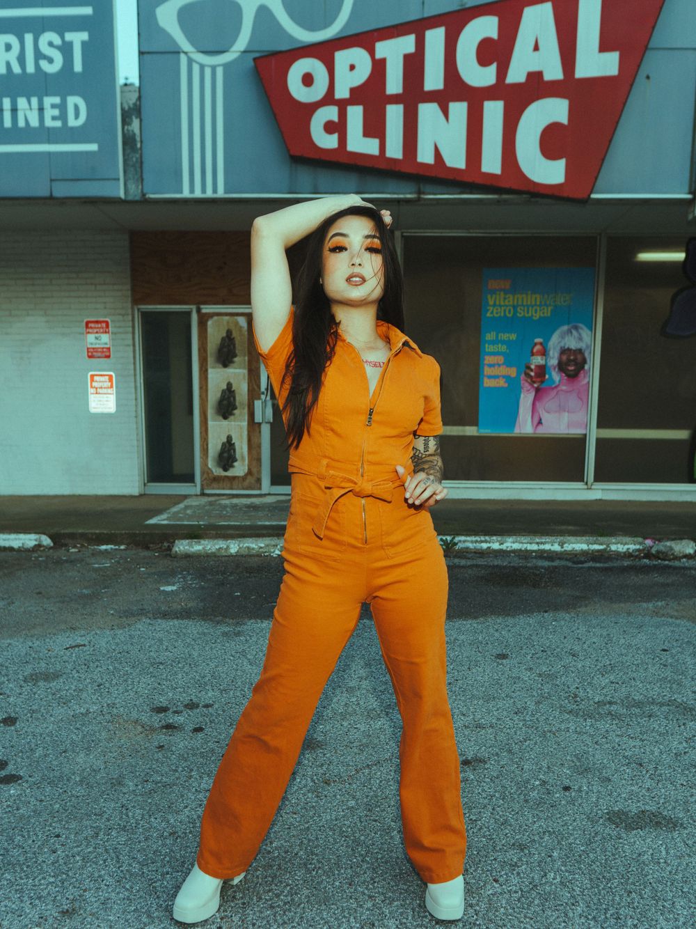 Model in bright orange jumpsuit poses stylishly outside optical clinic wearing white platform shoes.