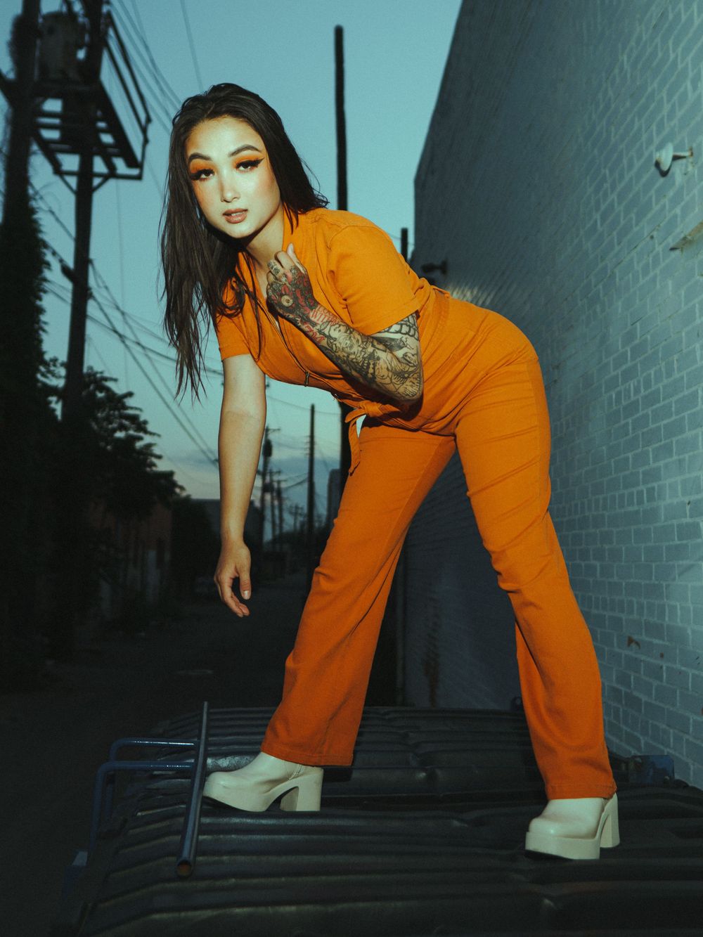 Urban fashion shoot on dark stairs with model in striking orange jumpsuit at dusk.