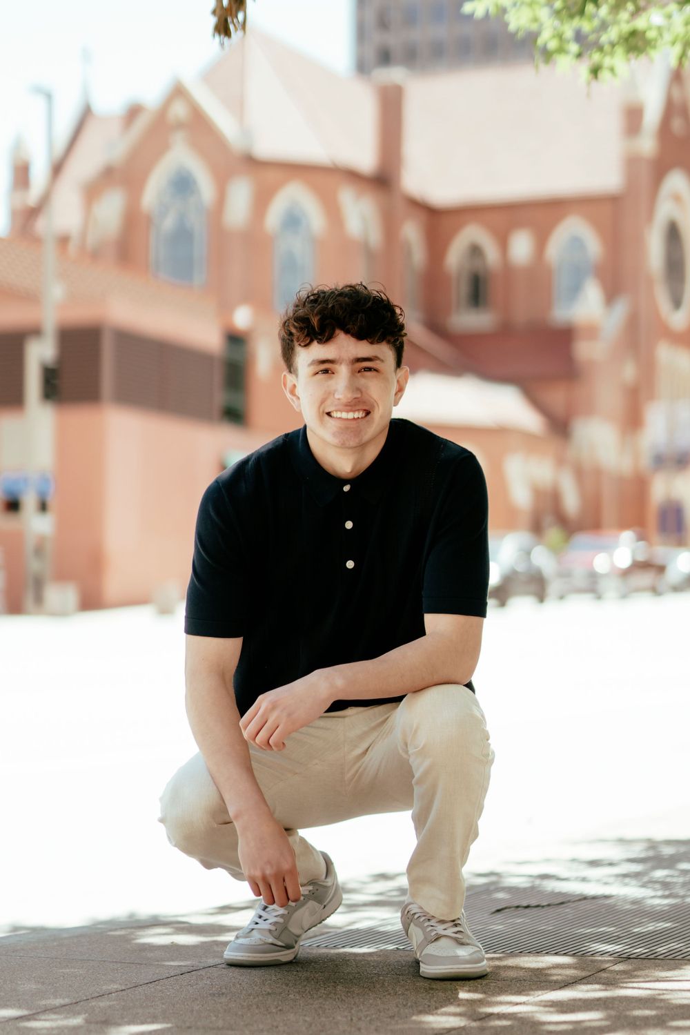 Casual portrait in front of a brick church with gothic arched windows.