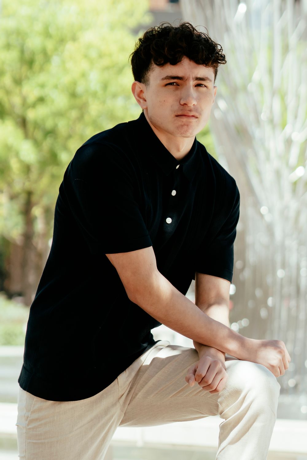 Portrait shot outdoors featuring black polo shirt and khaki pants against natural lighting.