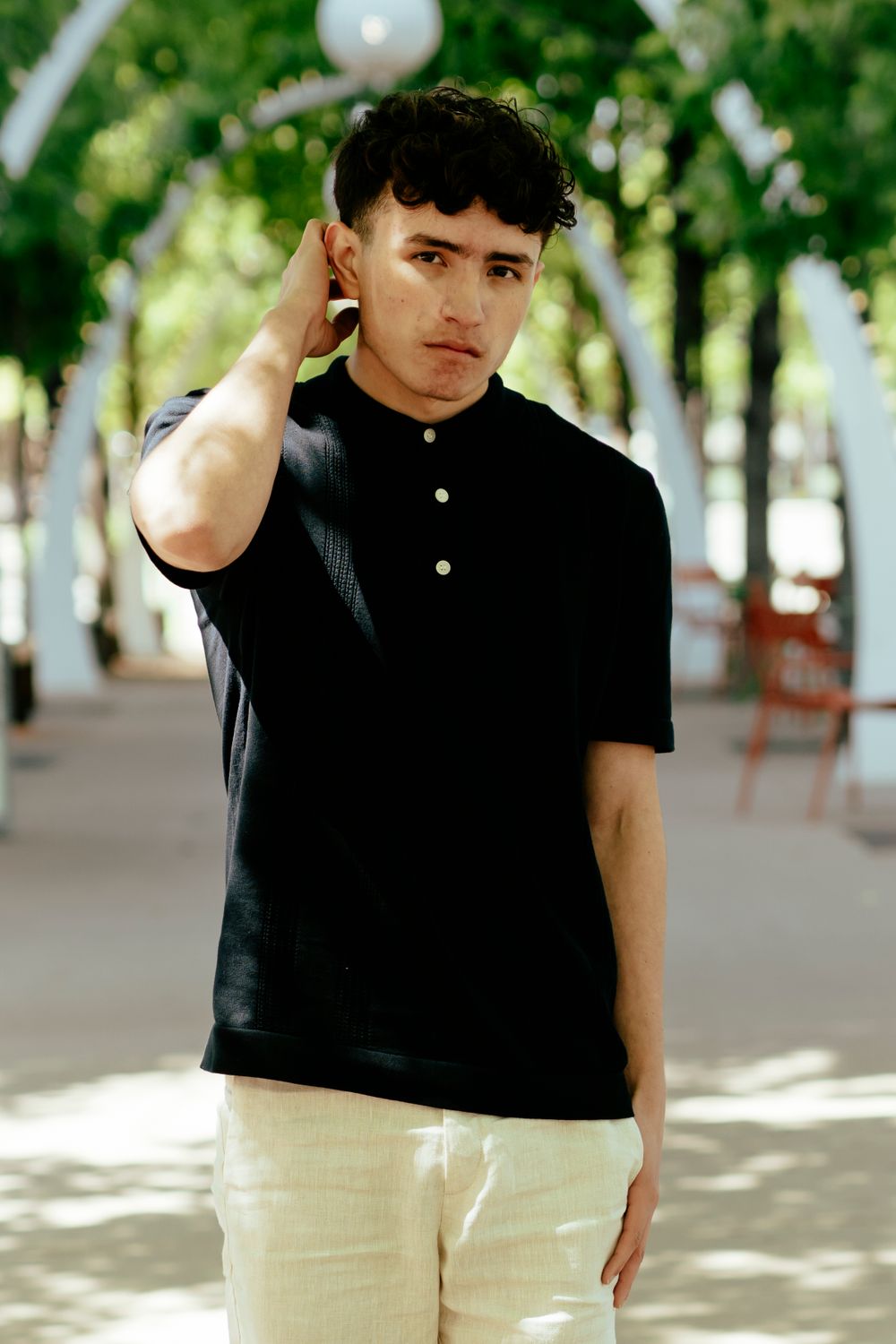 Stylish casual portrait with trees and dappled sunlight in background.