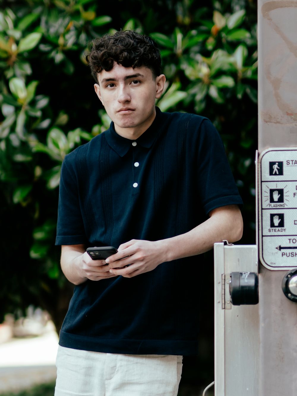 Casual portrait next to a vintage pay phone with foliage in background.