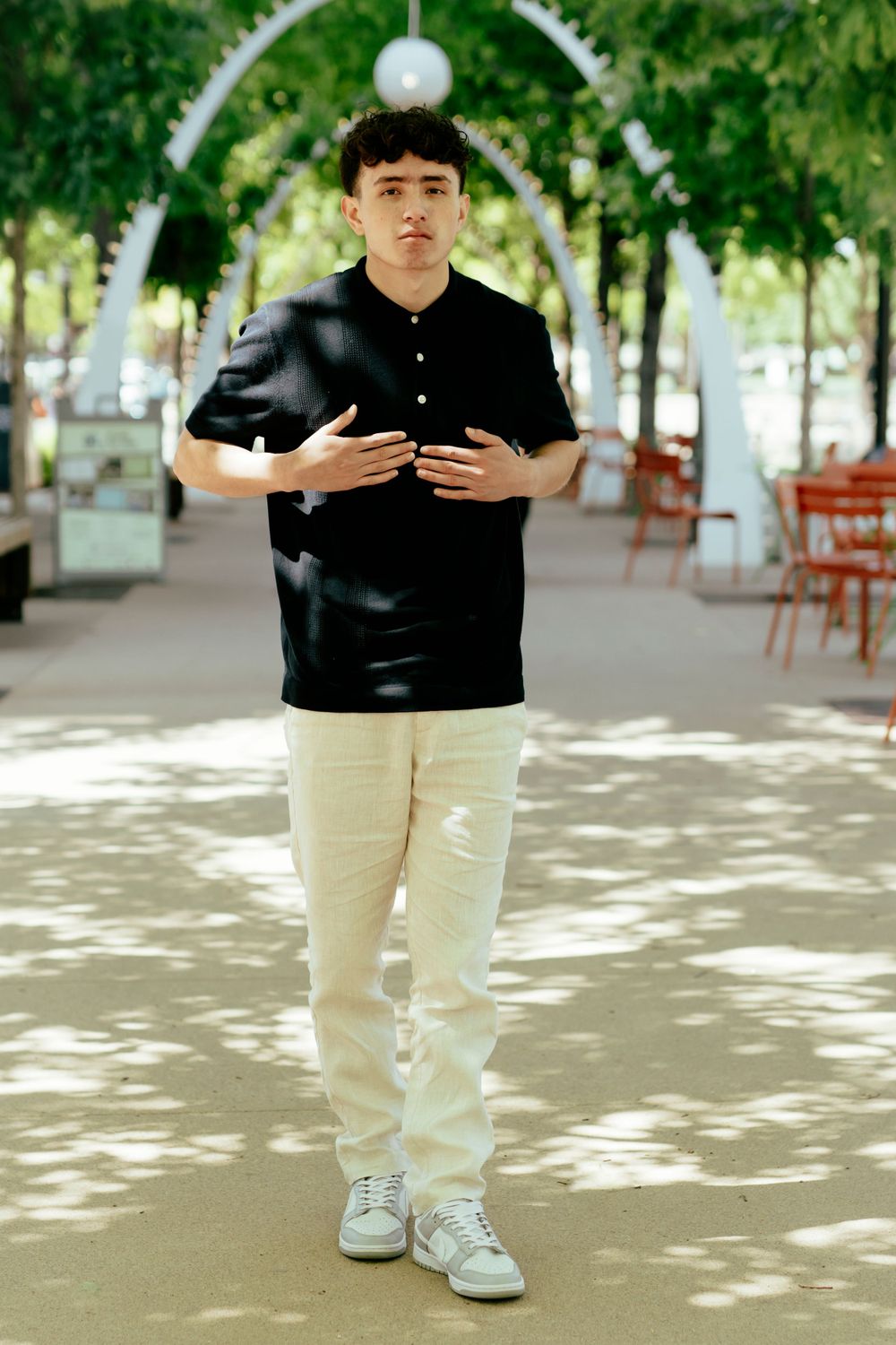 Standing portrait under decorative arches with string lights and trees.