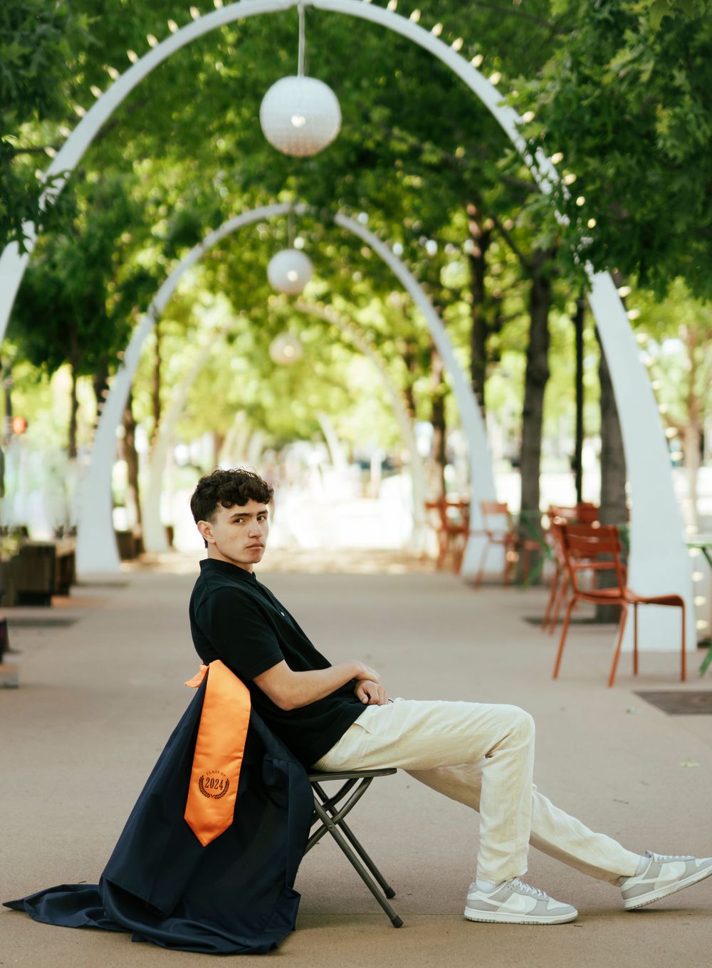 Seated portrait with orange bag under white arched walkway with hanging lights.