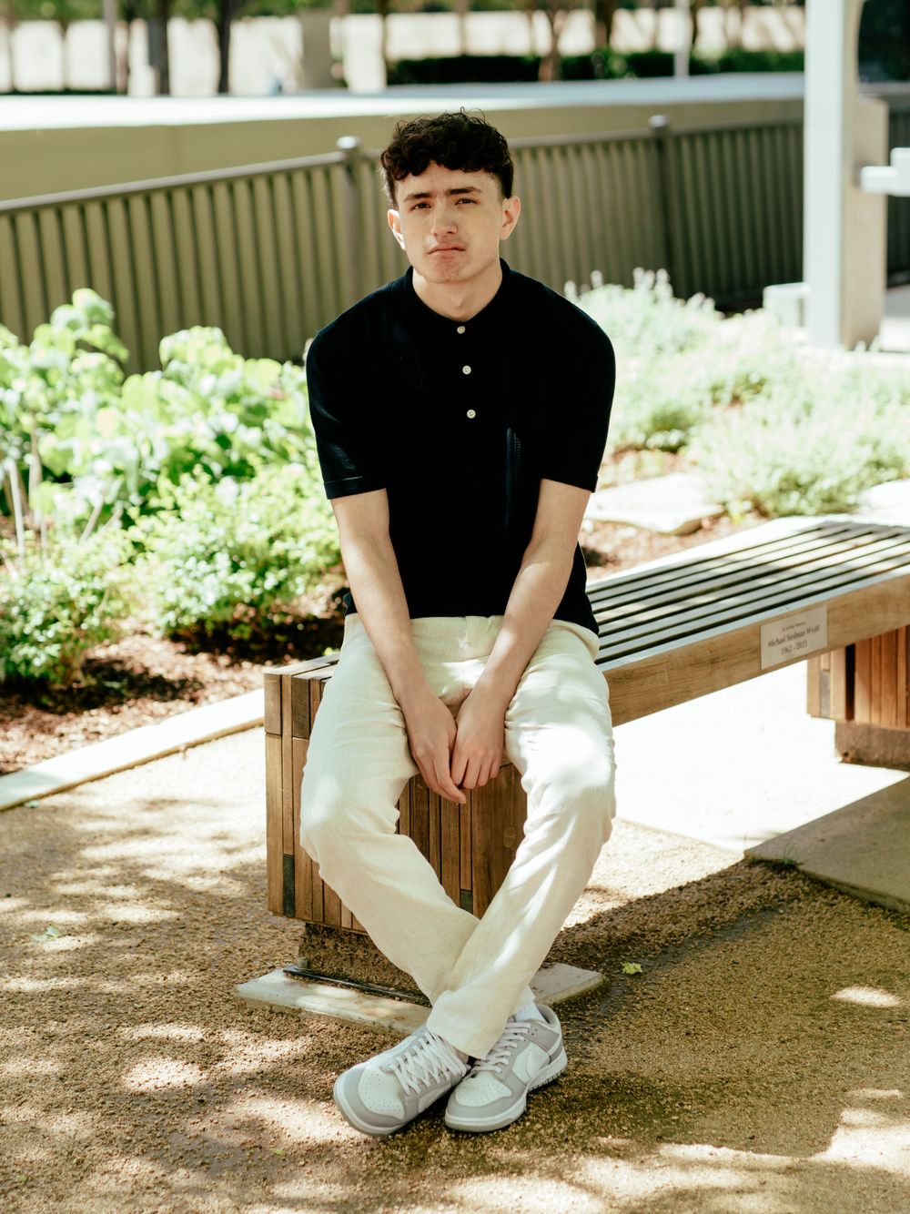 Casual outdoor portrait on wooden bench with landscaped garden in background.