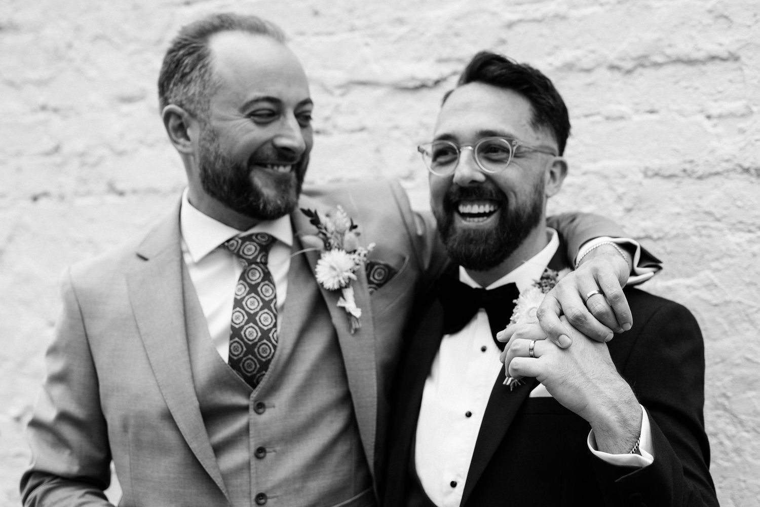 Black and white wedding portraits showing joyful moments against a textured wall.