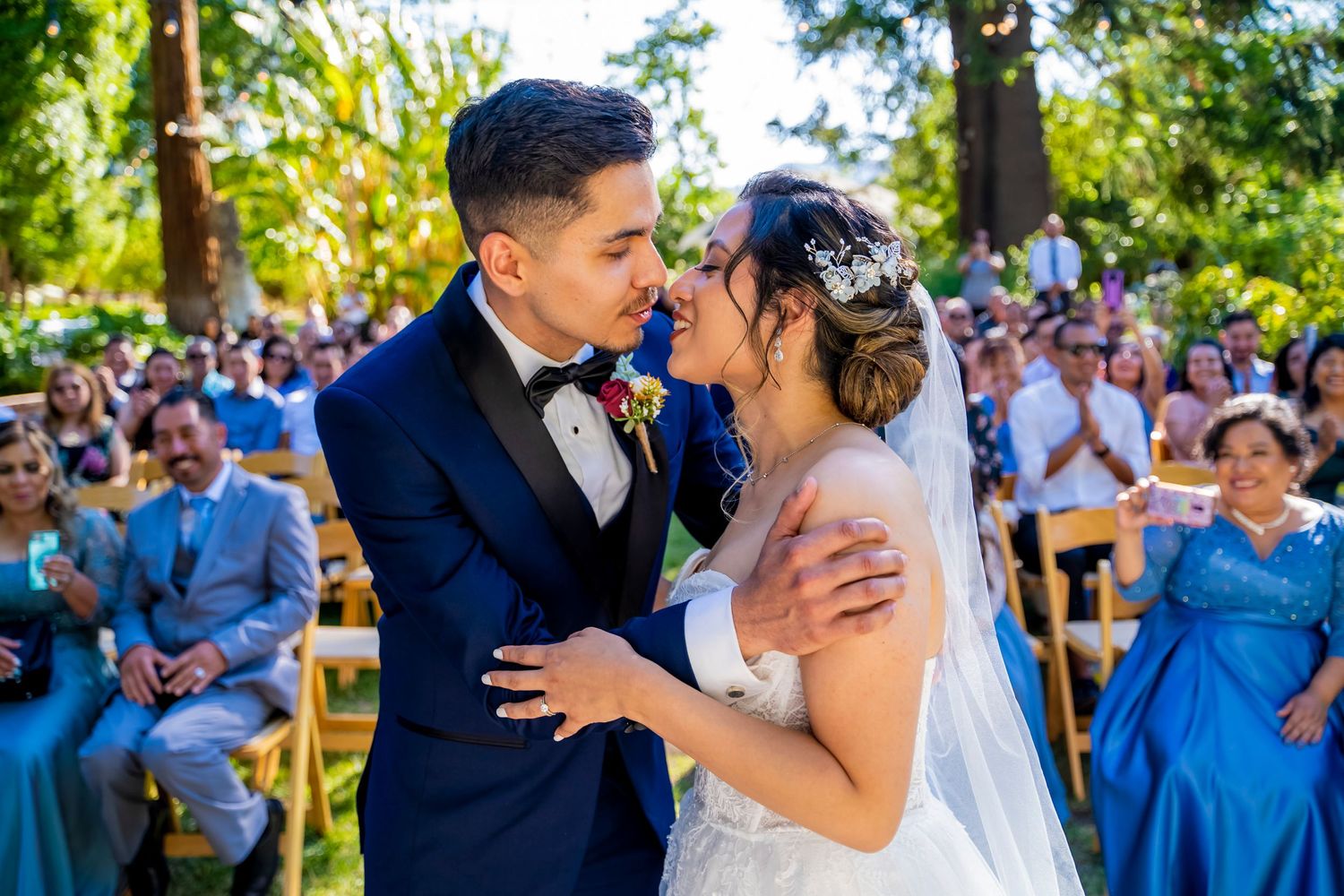 A tender moment during an outdoor wedding ceremony surrounded by guests in a garden setting. riverside.