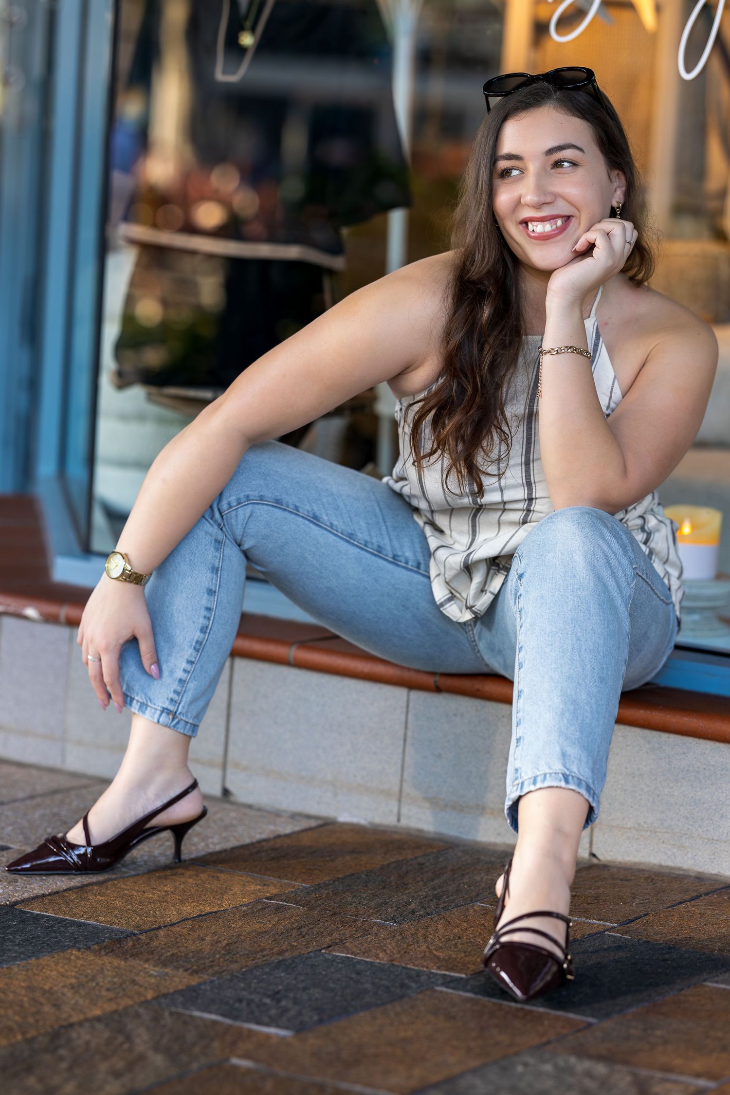 Woman in blue jeans and black heels sitting casually on stone steps in an urban setting.