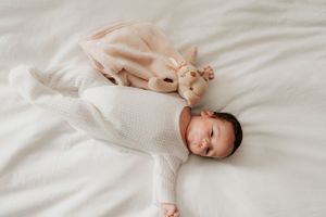 Sleeping baby in white sweater lying on bed next to plush toy.