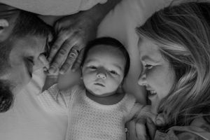 Black and white intimate family portrait with baby lying between parents.