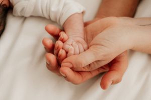 Close-up of tiny baby hand being tenderly held by adult hands on white fabric.