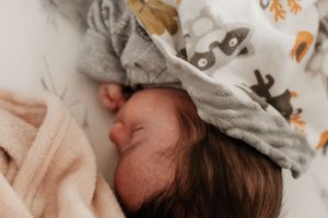 Newborn baby sleeping in gray and peach patterned blanket.