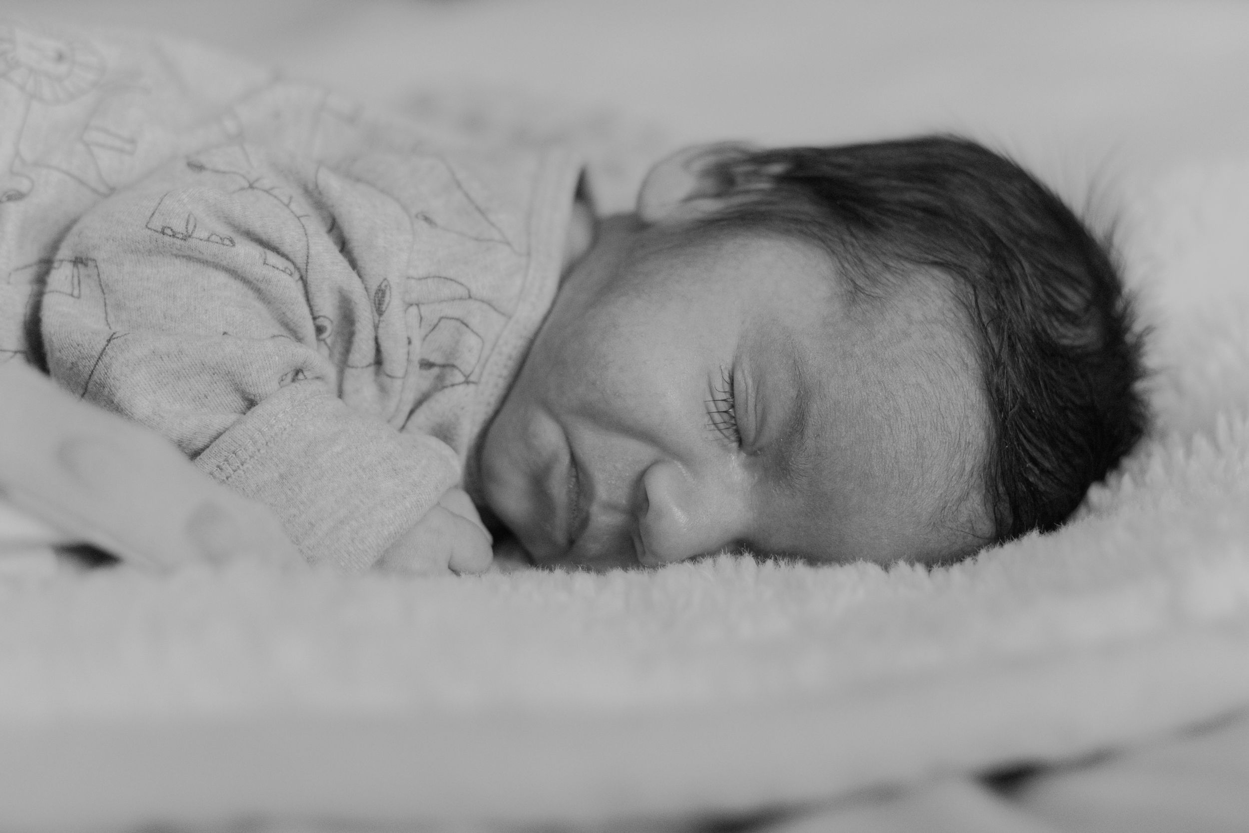 Black and white portrait of sleeping newborn wrapped in soft blanket.