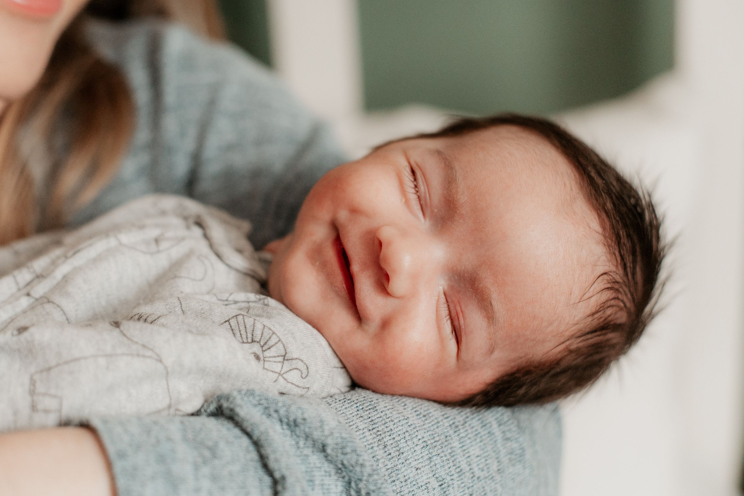 Newborn baby sleeping peacefully in soft gray clothing.