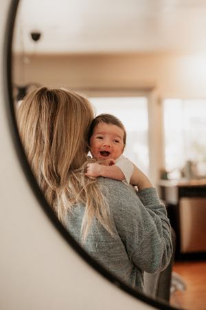 Mirror reflection captures a tender moment of parent holding a smiling baby in a cozy home setting.