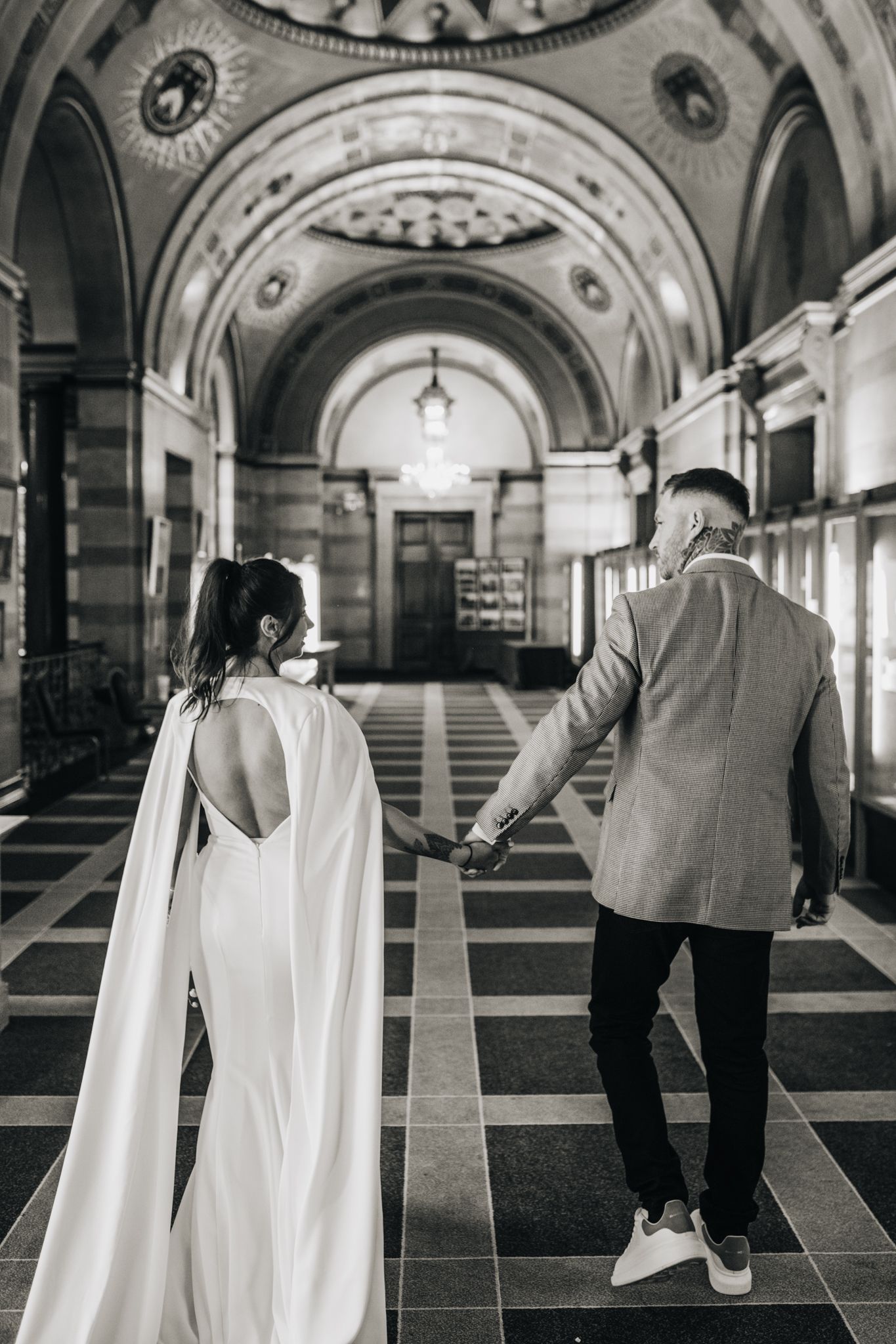 Couple walks through an elegant arched hallway with classic architecture.