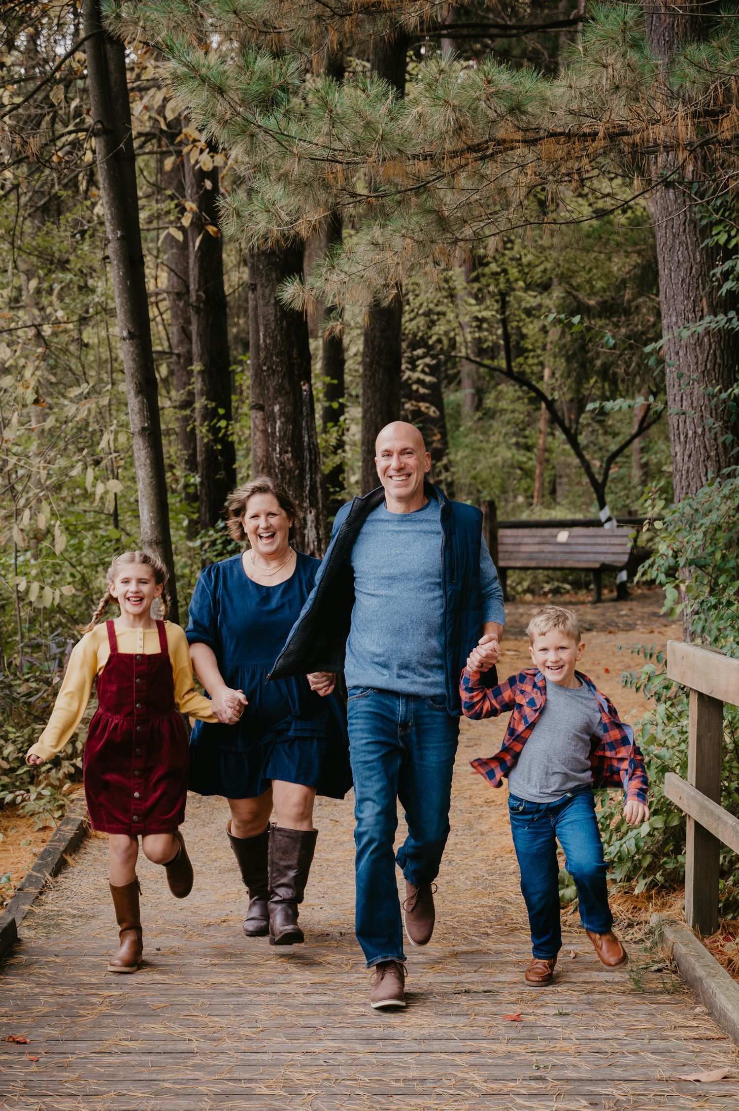 Happy family of four running and laughing on a wooden boardwalk path through a forest in autumn.