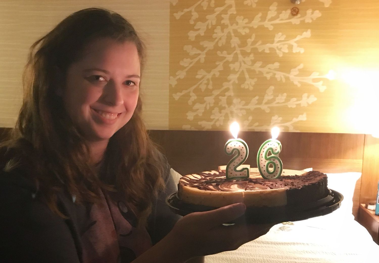 A birthday celebration with a chocolate cake featuring glowing number 26 candles.